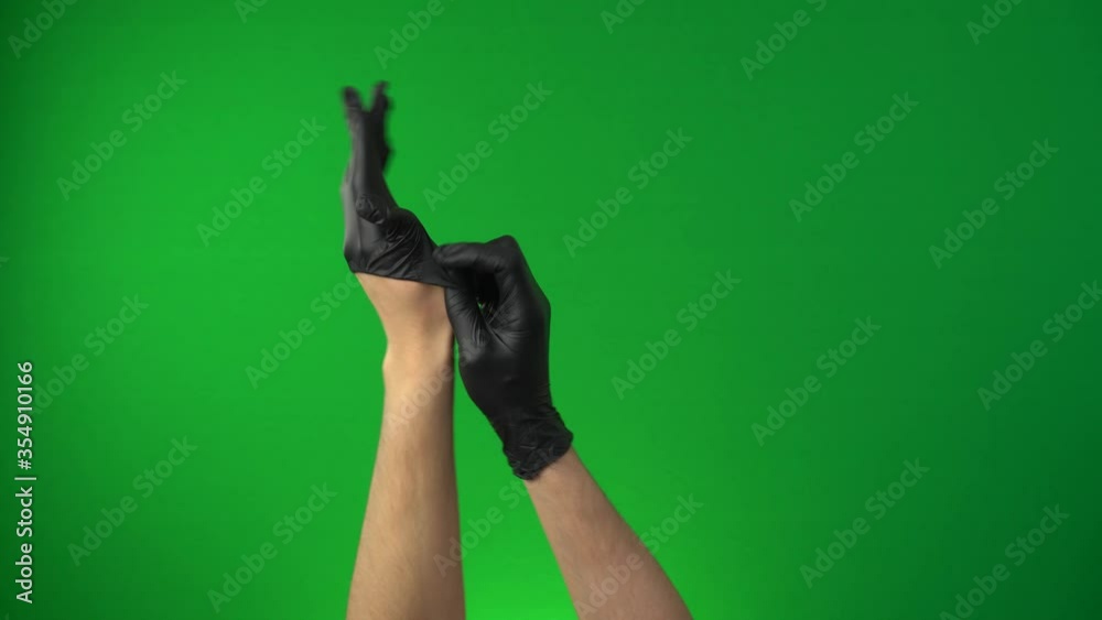 Man puts on gloves. Coronavirus pandemic, Covid-19. Hands in a black medical glove isolated on a chroma key green screen background