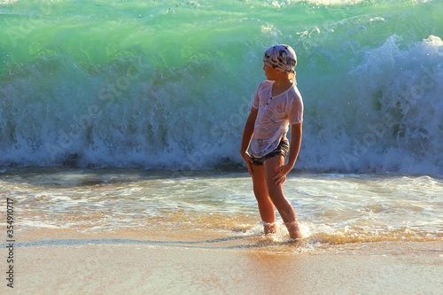 Cute european boy watching for huge ocean wave and having fun on seashore of tropical island.