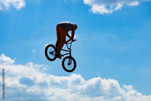 Silhouette of a man jumping on a Bicycle against a blue sky with white clouds.