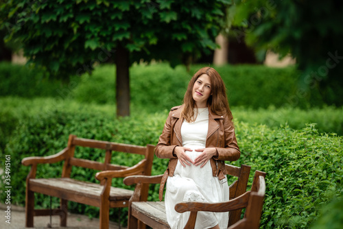 Beautiful pregnant woman sitting in the park on the bench.