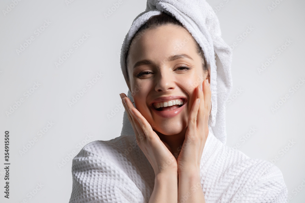 Happy laughing young woman wearing bathrobe and head towel with nude makeup touching face. - obrazy, fototapety, plakaty 