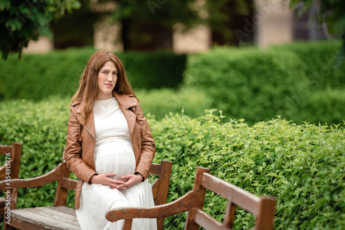 Beautiful pregnant woman sitting in the park on the bench. © lialia699