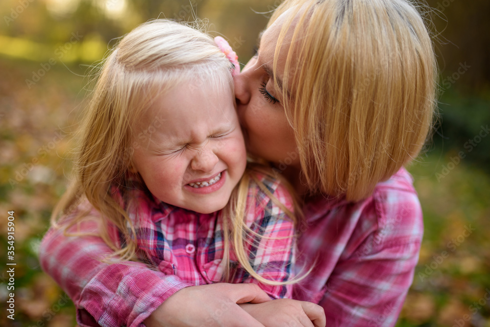 Mom and daughter in pink shirts. A woman kisses a girl. The girl is crooked. Close-up. Mom and daughter in pink shirts. A woman kisses a girl. The girl is crooked. Close-up.