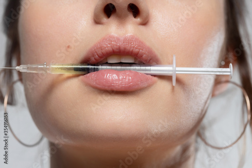Closeup female mouth holding syringe with needle and liquid filler. 