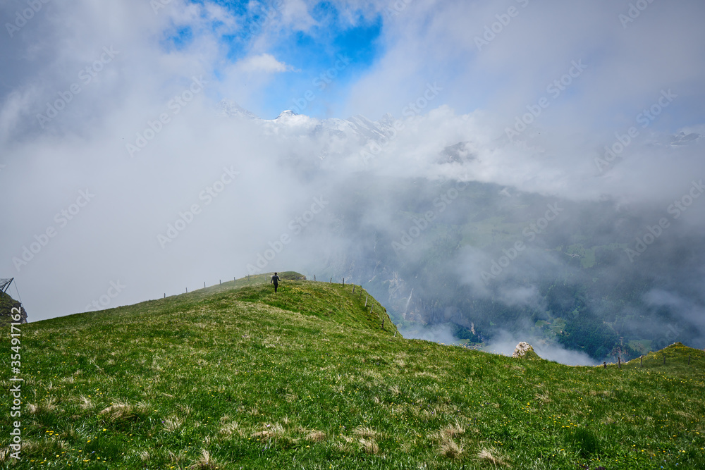 Clouds covering snowy mountains. Swiss Alps landscape with meadow and green nature. Taken in Männlichen, Grindelwald mountains, Bernese Alps, Switzerland. Clouds covering snowy mountains. Swiss Alps landscape with meadow and green nature. Taken in Männlichen, Grindelwald mountains, Bernese Alps, Switzerland.