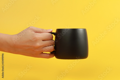 Female hand holding a coffee mug isolated on yellow background photo