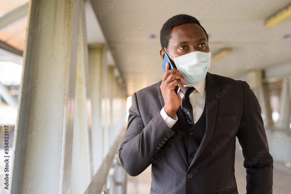 Portrait of African businessman with mask talking on the phone at the footbridge