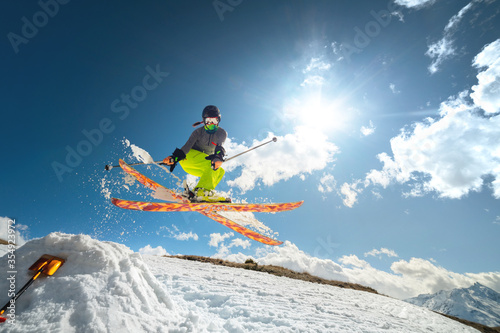 Girl skier in flight after jumping from a kicker in the spring against sun and blue sky. Close-up wide angle.