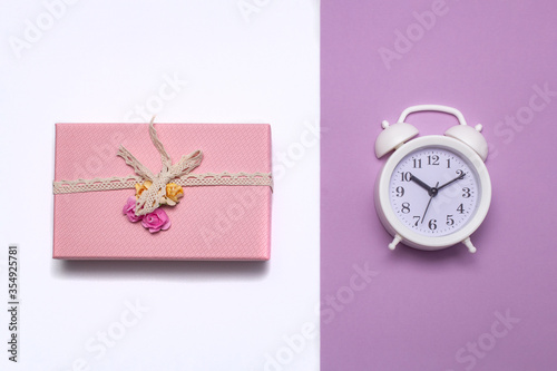 pink gift box wrapped with vintage ribbon on a light background and a white alarm clock on a pink 