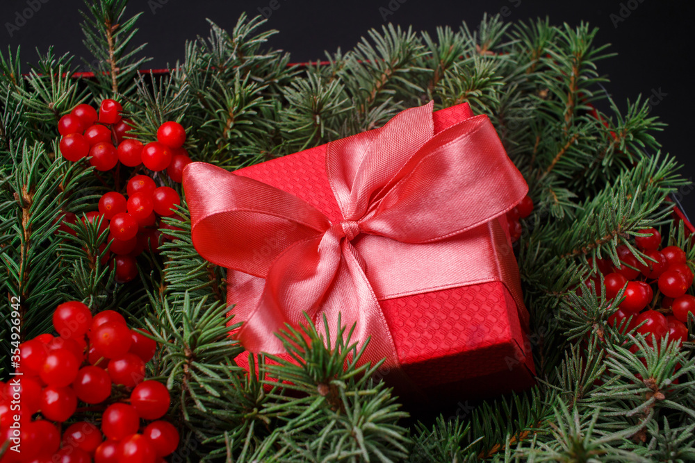 New Year Christmas Xmas holiday celebration red present gift box with satin pink bow, immersed in the needles of a Christmas tree decorated with red berries. Dark festive composition. New Year Christmas Xmas holiday celebration red present gift box with satin pink bow, immersed in the needles of a Christmas tree decorated with red berries. Dark festive composition.