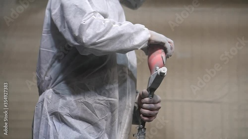 Powder coating of metal products. A man in a White protective and respirator suit pours grey powder into a spray gun in the paint chamber