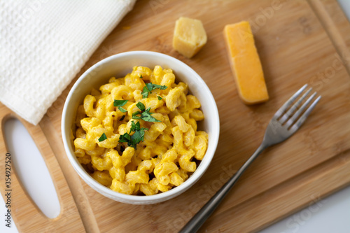 Traditional American macaroni and cheese comfort food (also called mac n cheese) with elbow pasta coated in a cheesy creamy cheddar sauce. Topped with parsley, cheese in the background.
