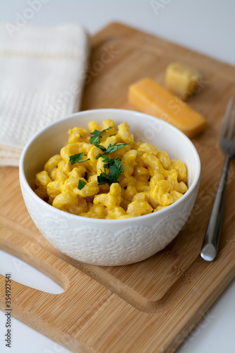 Traditional American macaroni and cheese comfort food (also called mac n cheese) with elbow pasta coated in a cheesy creamy cheddar sauce. Topped with parsley, cheese in the background.
