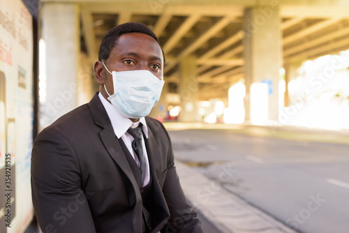 African businessman with mask sitting and waiting at the bus stop