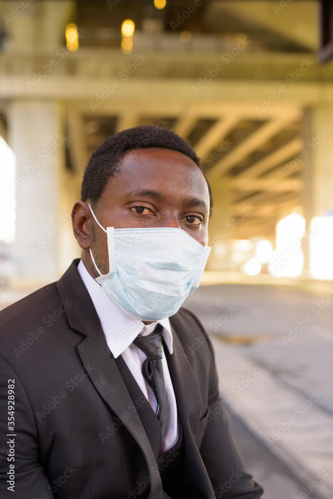 African businessman with mask sitting at the bus stop in the city African businessman with mask sitting at the bus stop in the city