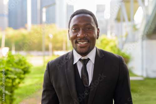 Face of happy handsome bearded African businessman in suit smiling at the park