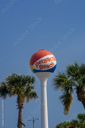 Iconic Pensacola Beach beachball water tower standing above palm trees with a blue sky behind it