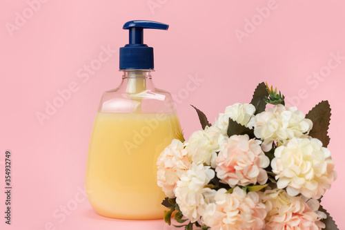 Yellow liquid soap bottle and beautiful delicate flowers on a pink background. Clean hands concept. Shampoo, Liquid Soap, Aromatic Bath Salt And Other Toiletry.
