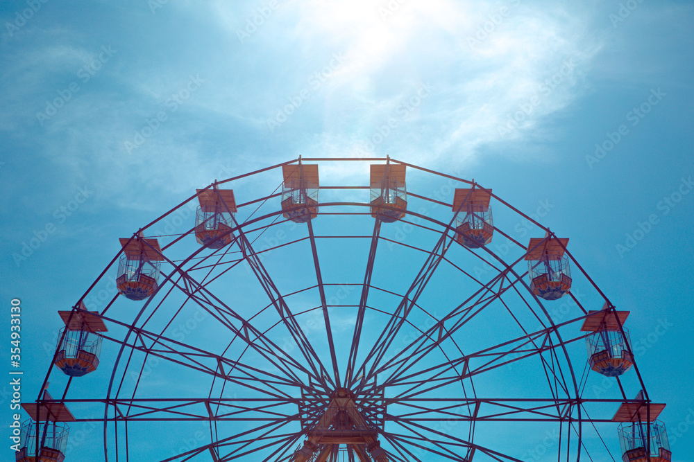 A symmetrical view of the top half of a vintage Ferris Wheel fairground ride with blue sky background and copy space