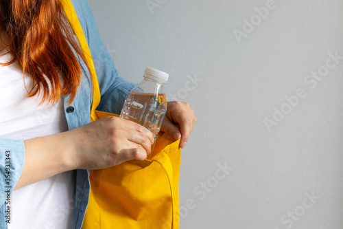 Fototapeta A young girl in a white T-shirt takes out a plastic bottle of water from a yello