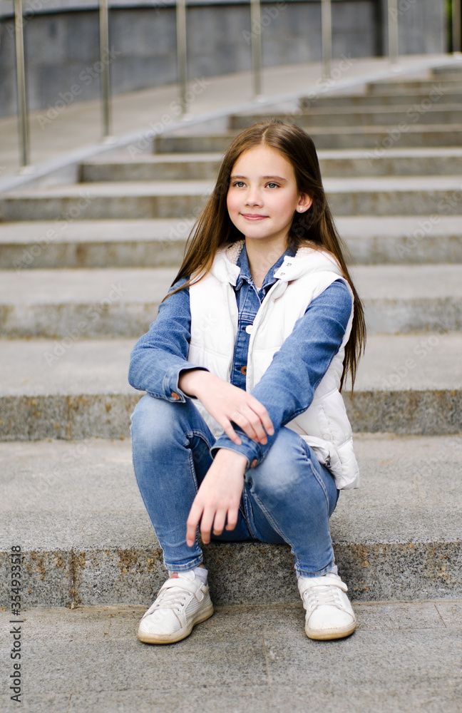 Adorable smiling little girl child preteen sitting on the steps
