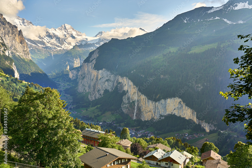 Lauterbrunnen Valley at sunset with snowy mountains, waterfall and green nature. Landscape panorama taken from mountain village Wengen, Switzerland