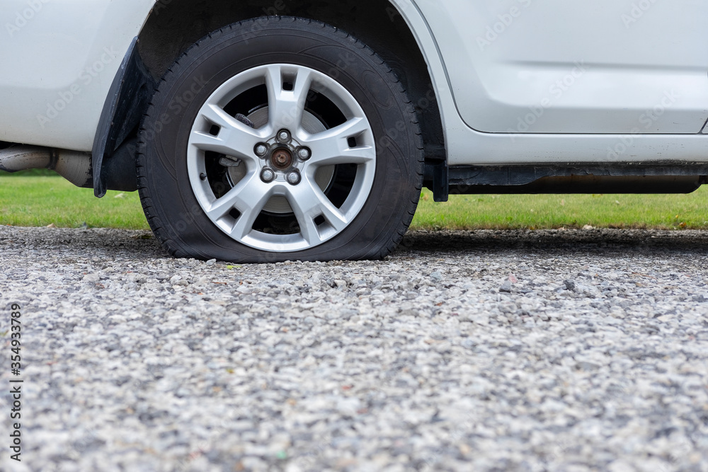 Close up of flat rear tire of white SUV track car vehicle automobile punctured by nail. Summer day, residential street. Selective focus, depth of field, space for copy.