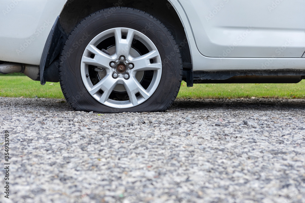 Close up of flat rear tire of white SUV track car vehicle automobile punctured by nail. Summer day, residential street. Selective focus, depth of field, space for copy. Close up of flat rear tire of white SUV track car vehicle automobile punctured by nail. Summer day, residential street. Selective focus, depth of field, space for copy.