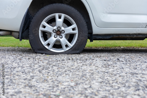 Close up of flat rear tire of white SUV track car vehicle automobile punctured by nail. Summer day, residential street. Selective focus, depth of field, space for copy. © Elena Berd