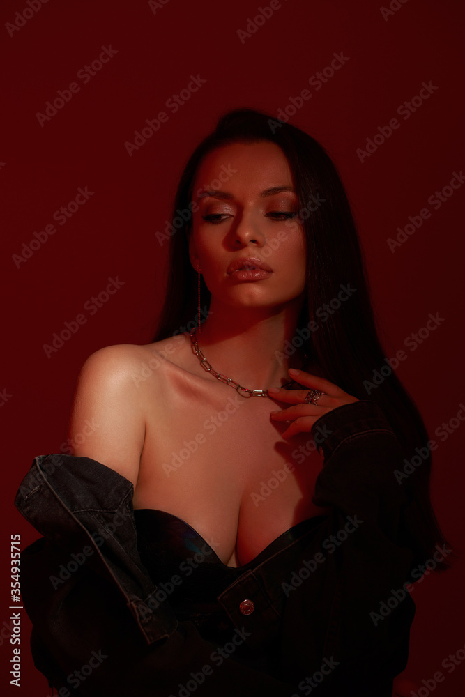 Fashion breast up portrait of young sexy woman with perfect makeup and long dark straight hair posing on red background. Sylish girl wearing top and jacket Fashion breast up portrait of young sexy woman with perfect makeup and long dark straight hair posing on red background. Sylish girl wearing top and jacket