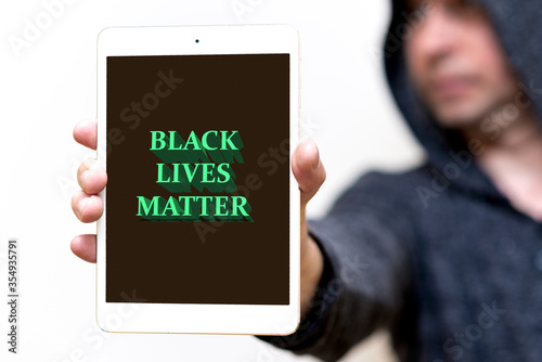 Portrait of a hooded white man holds tablet with the inscription Black Lives Matter. protests of racial discrimination.White studio wall.