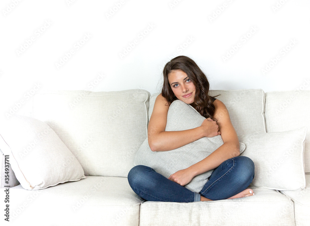 Beautiful young model with brown hair posing on white couch.