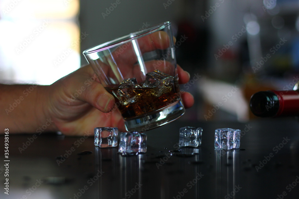 whiskey on ice cubes in whiskey glass in hand,with some ice cubes  whiskey on table.