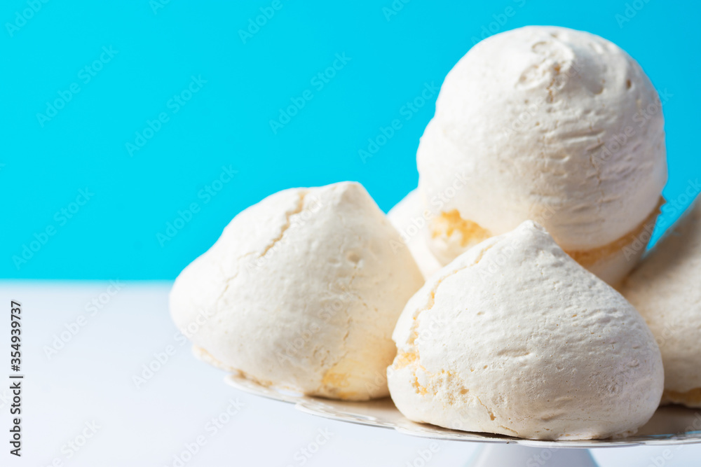 Home baked meringue cookies on white cake stand on blue white background. French Italian Swiss desserts. Baking poster template