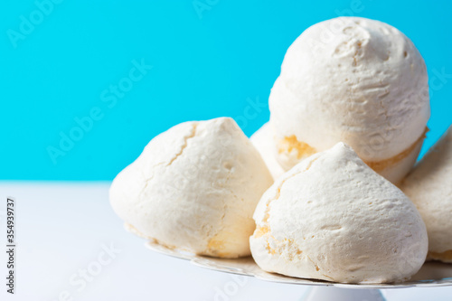 Home baked meringue cookies on white cake stand on blue white background. French Italian Swiss desserts. Baking poster template