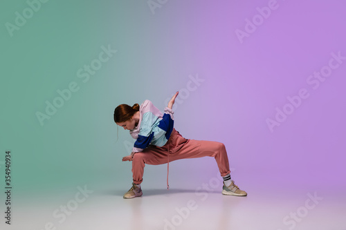 Beautiful sportive girl dancing hip-hop in stylish clothes on colorful gradient background at dance hall in neon light. Youth culture, movement, style and fashion, action. Fashionable bright portrait.