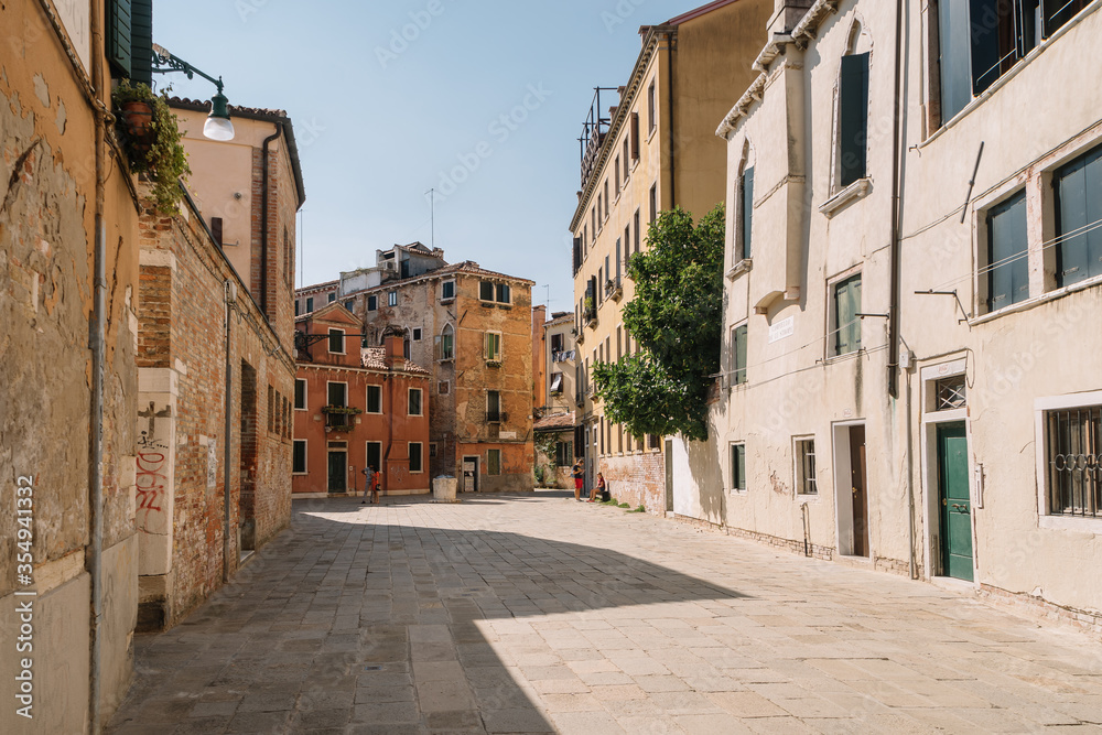 Tourists are walking along the narrow and bright streets of sunny Venice, Italy.