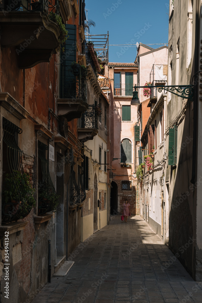 One woman is walking along the narrow and bright street of sunny Venice, Italy.