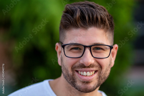 young man with glasses smiling in the open park