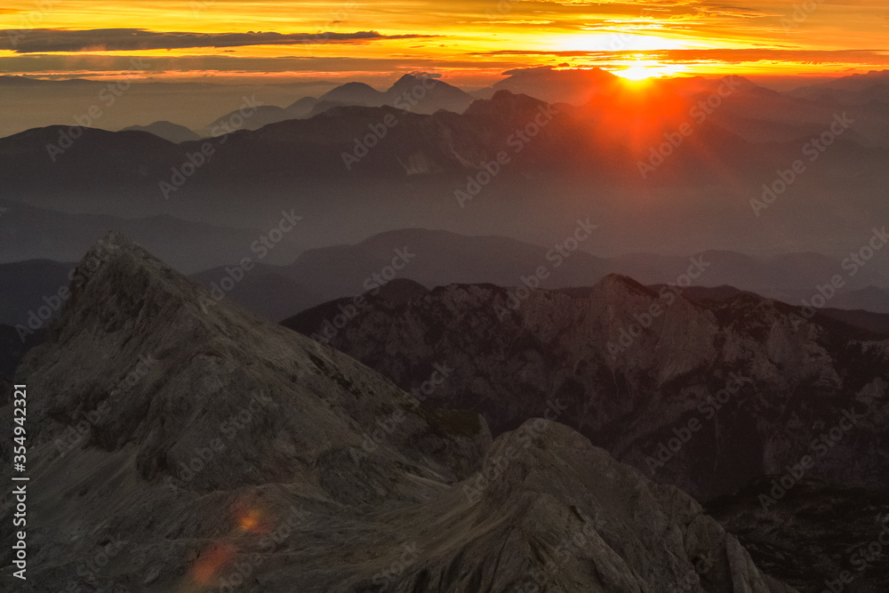 Early morning viewed from Triglav, the highest mountain in Slovenia just at dawn. Visible sun rising and shining above the valleys and mountain ranges in front