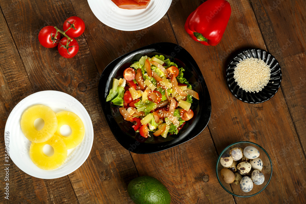 Pan-Asian salad with in a black plate and a row of ingredients on a wooden table. Pan-Asian salad with in a black plate and a row of ingredients on a wooden table.