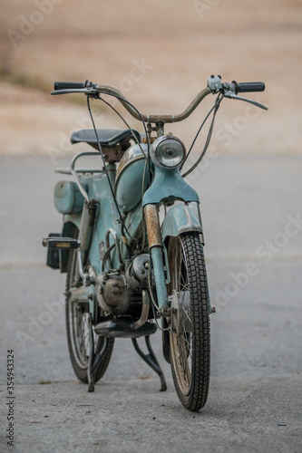 Frontal view of an old blue moped or scooter from the 1950 or fifties. Retro vintage moped parked on asphalt parking lot. photo