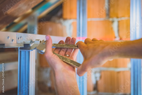 Drywall plaster stud crimpers in action. A person holding and using stud crimping tool in hand while building a metal drywall construction in a house during renovation