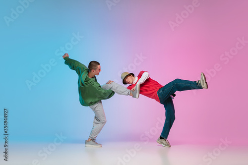 In action. Sportive boys dancing hip-hop in stylish clothes on colorful gradient background at dance hall in neon light. Youth culture, movement, style and fashion, action. Fashionable bright portrait