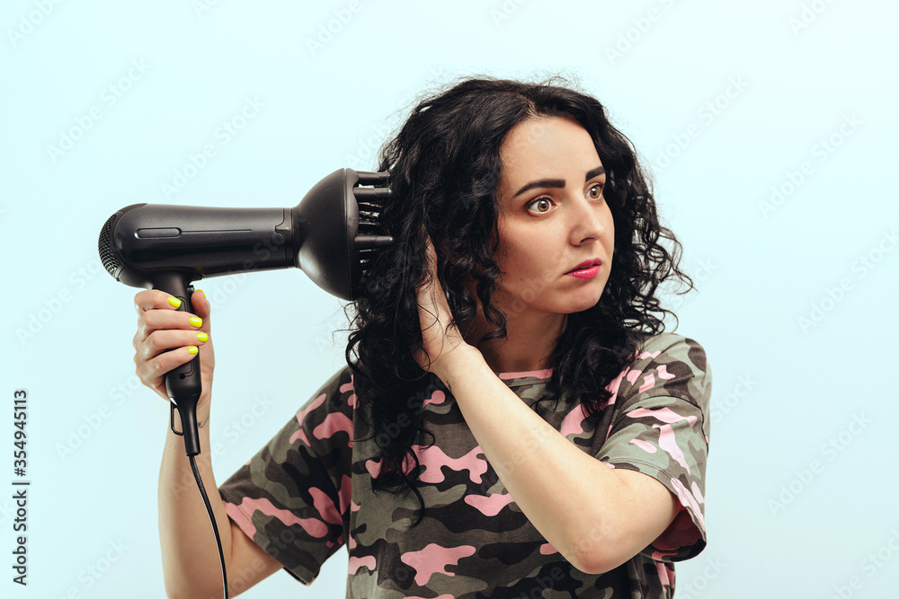 Woman styling her curly hair with hairdryer with special diffuser nozzle. Girl using a modern hairdryer.