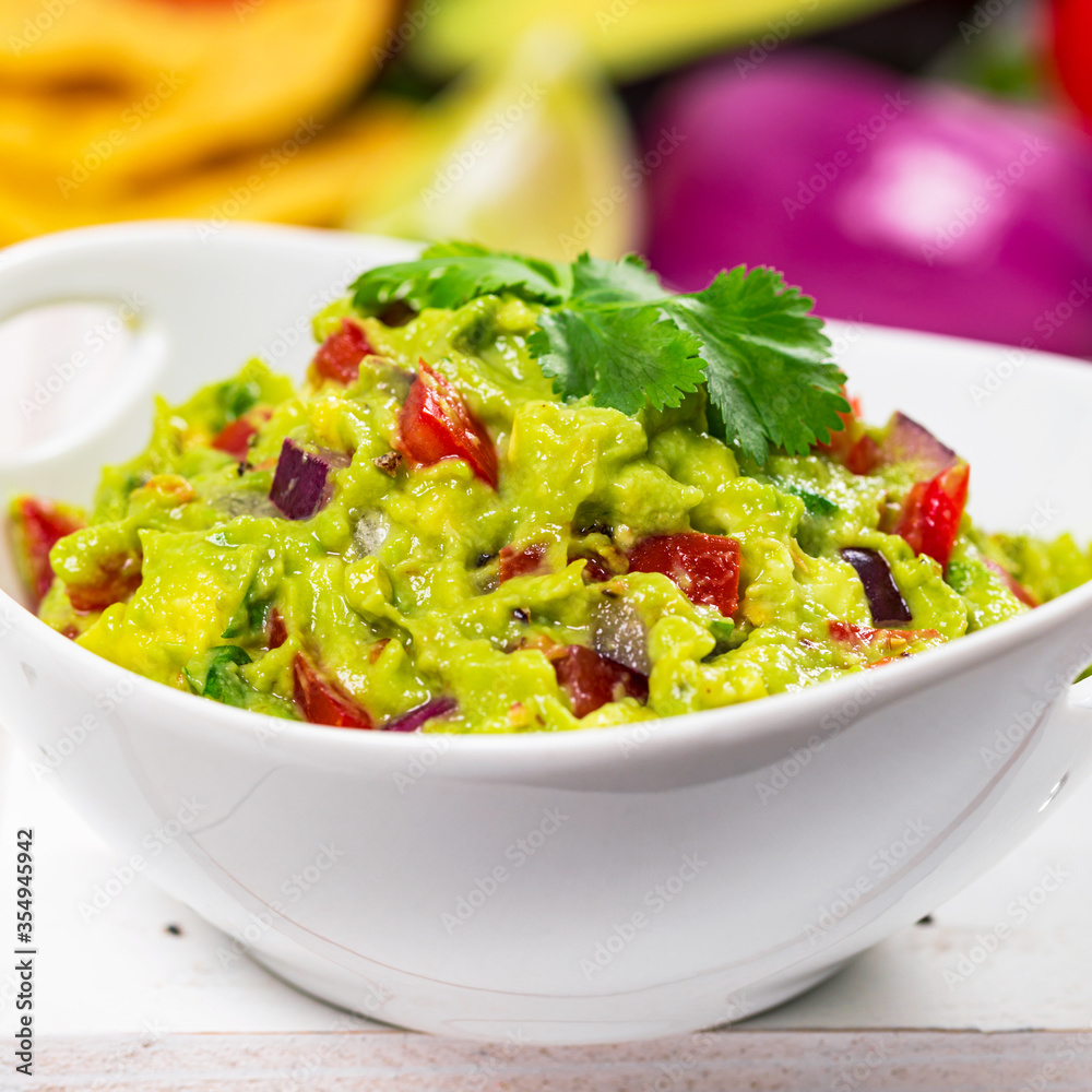 Bowl of Guacamole next to Fresh Ingredients on a Table with Tortilla Chips. Selective focus.