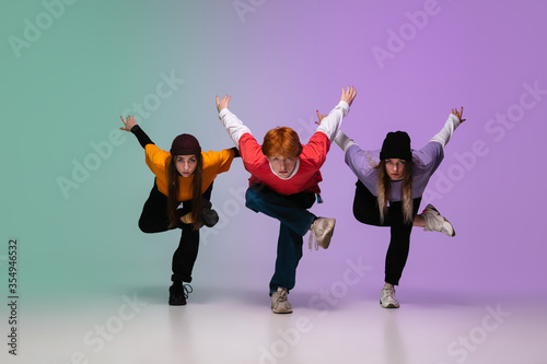 Group of teens, boys and girls dancing hip-hop in stylish clothes on colorful gradient studio background in neon light. Youth culture, movement, style and fashion, action. Fashionable portrait.