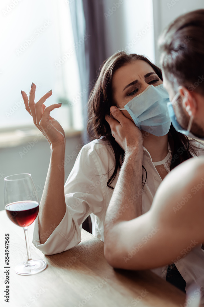 man with young displeased woman in medical mask at table