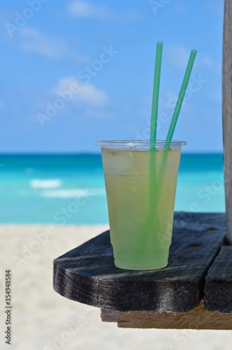 Cooled cocktail on a wooden table on Varadero beach in Cuba, the drink in a plastic mug with straws, blurred turquoise caribbean sea in the background, a sunny day