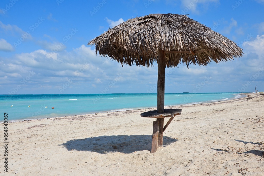 Straw parasol with table on the empty beach of Varadero in Cuba, turquoise caribbean sea in the background, blue sky